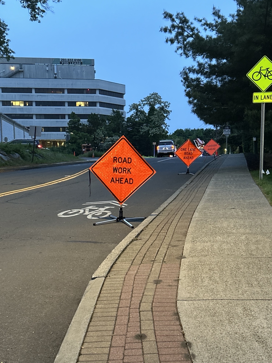Road work, one-lane road and flagger warning signs at dusk.