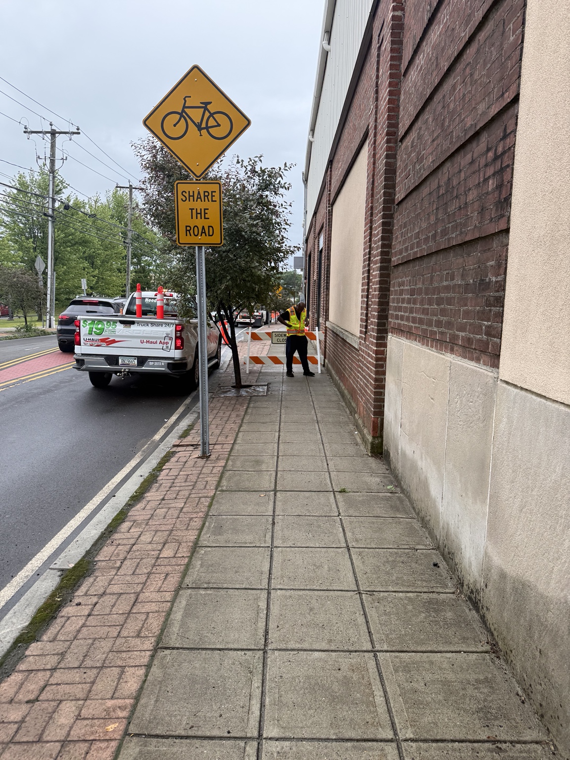 Crew member in high-visibility clothing beside a sidewalk barricade.